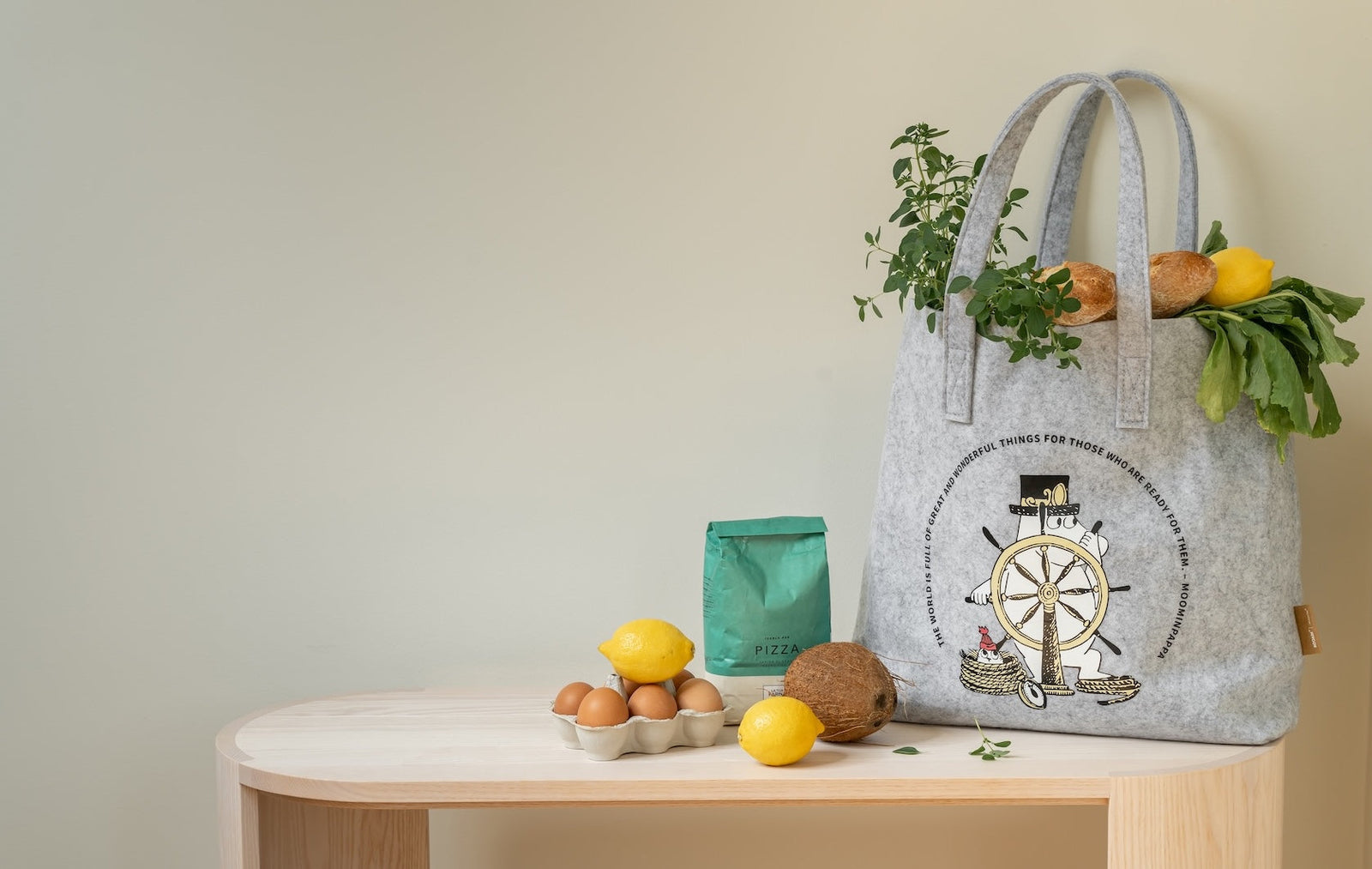 Moomin rPet Tote Bag, The Adventurer, filled with shopping, vegetable and fruits, etc.    The bag is shown on a bench with other bits of shopping already unpacked.