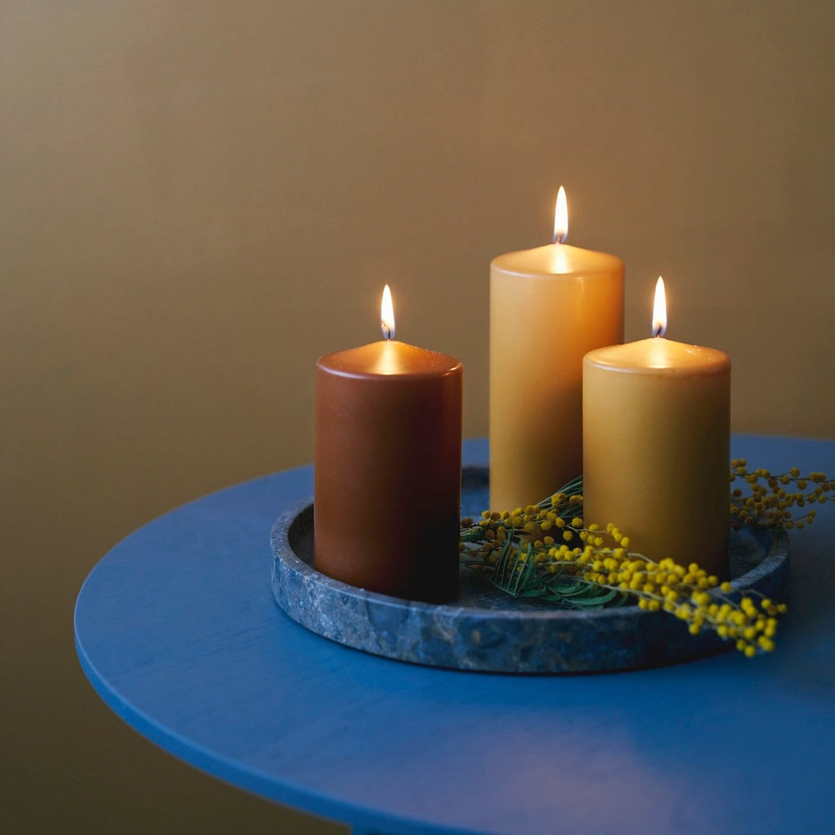 Lit Havi Pillar Candles in Saffron and Brown Colours, set on a blue table