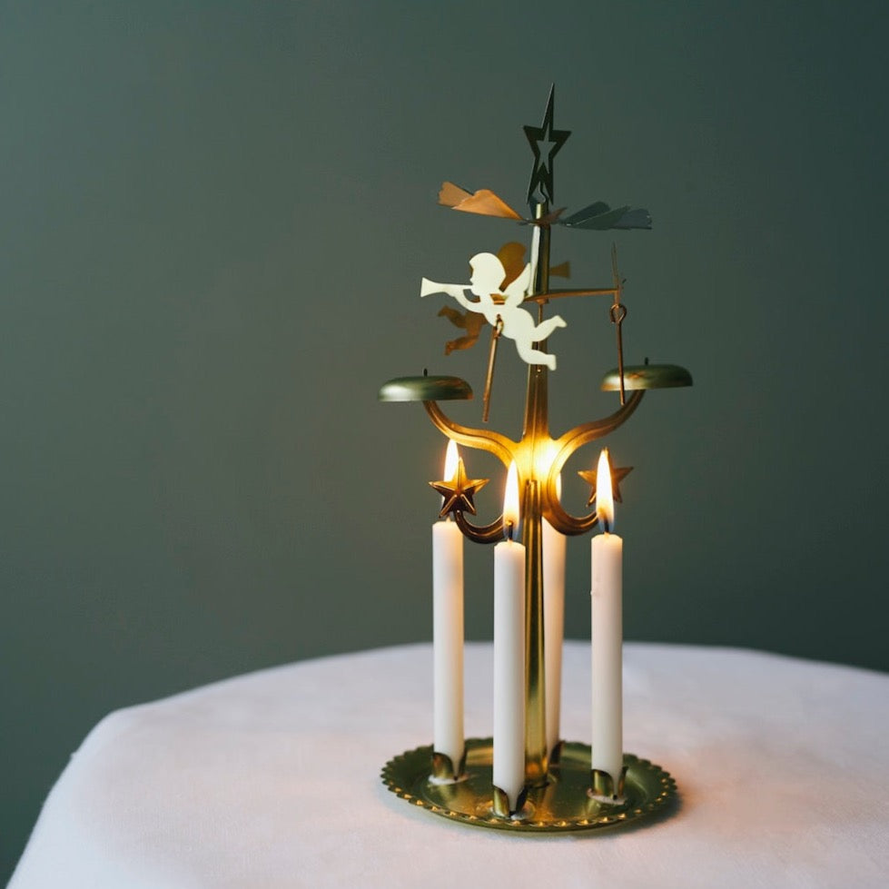  Gold spinning angel chime rotary with four lit white candles made by Havi in Finland,  on a round base, creating a warm glow against a dark background.