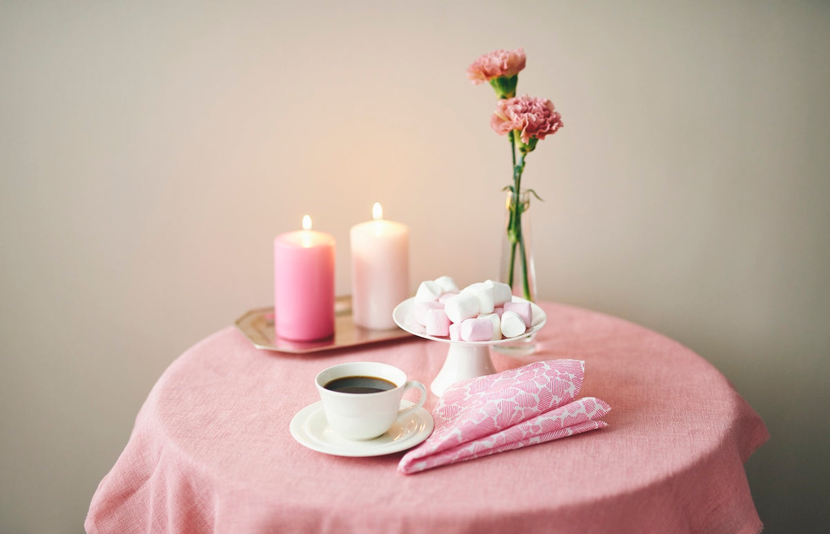 Havi Paper Napkins on a pink tablecloth, next to a cup off coffee and candles and a plate of marshmallows!