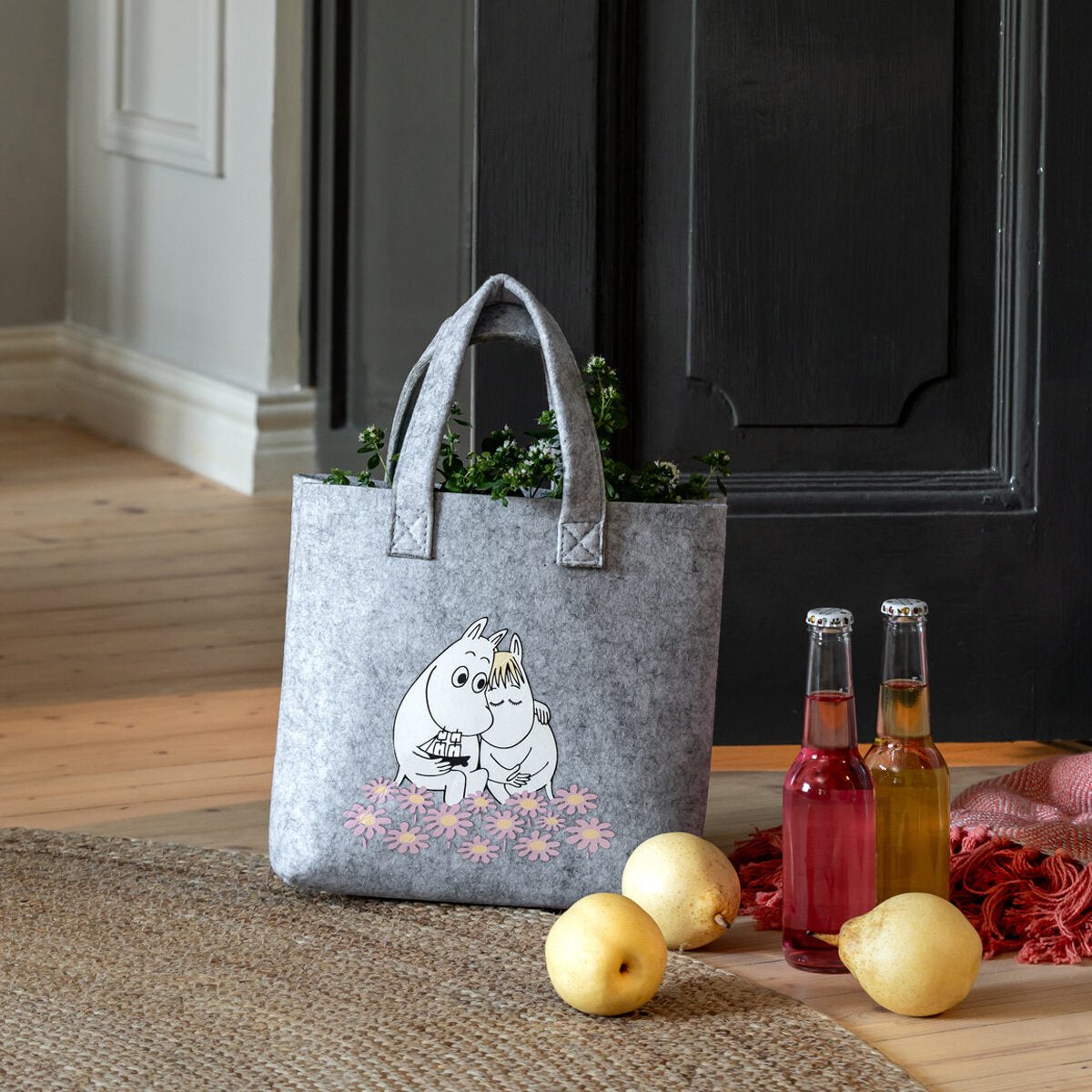 Moomin Together Tote Bag 25 x 25cm with herbs inside, sat on a wooden floor next to Lemons and juice bottles