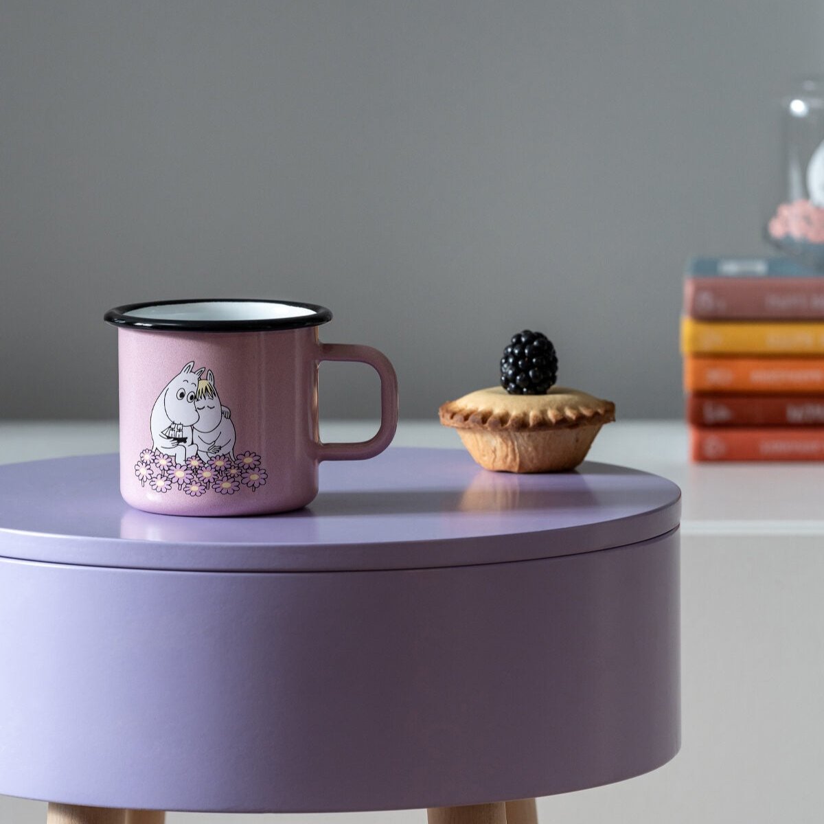 Muurla Moomin Together Enamel Mug shown on a lilac coloured table a small blackberry pie alongside!