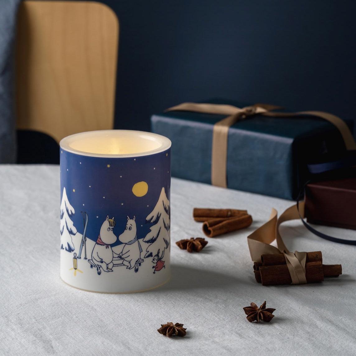 LED Candle with a Moomin winter design on a table with cinnamon sticks and pine cones.