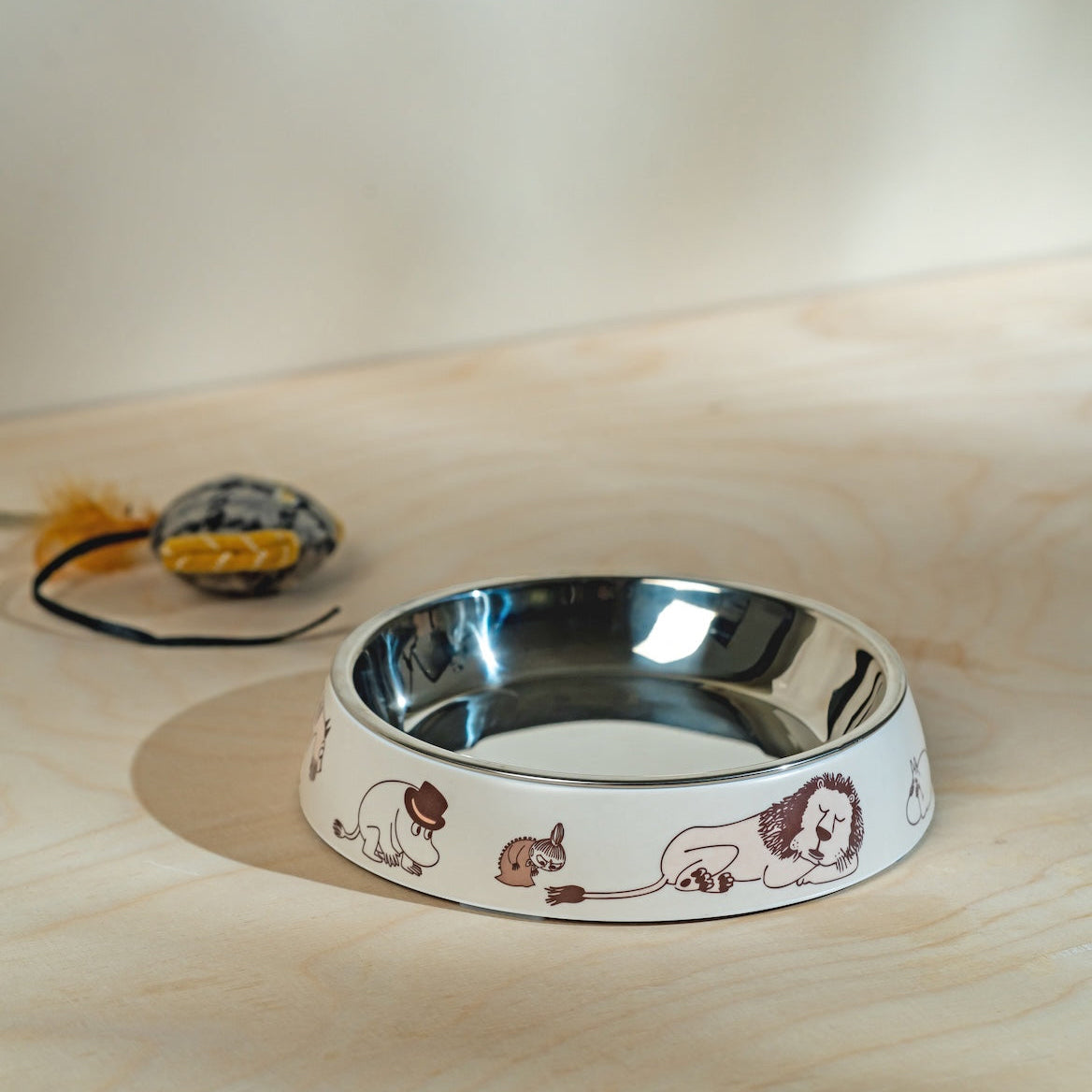 Stainless steel pet bowl with Moomin Moments designs on a wooden surface