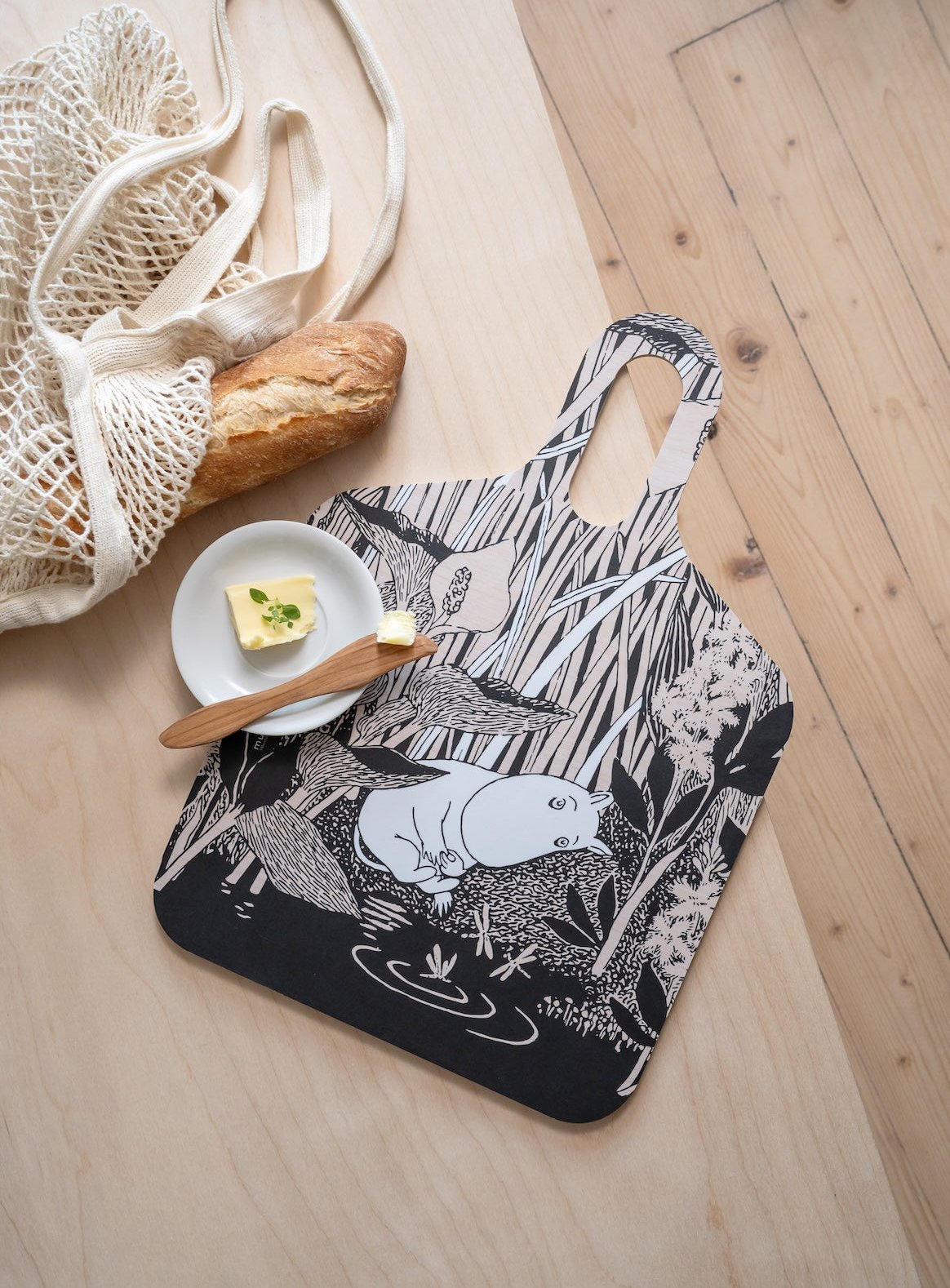 Moomin Chop and Serve Board on a kitchen table next to a shopping bag with bread and a little butter ready to be spread!  Muurla Design