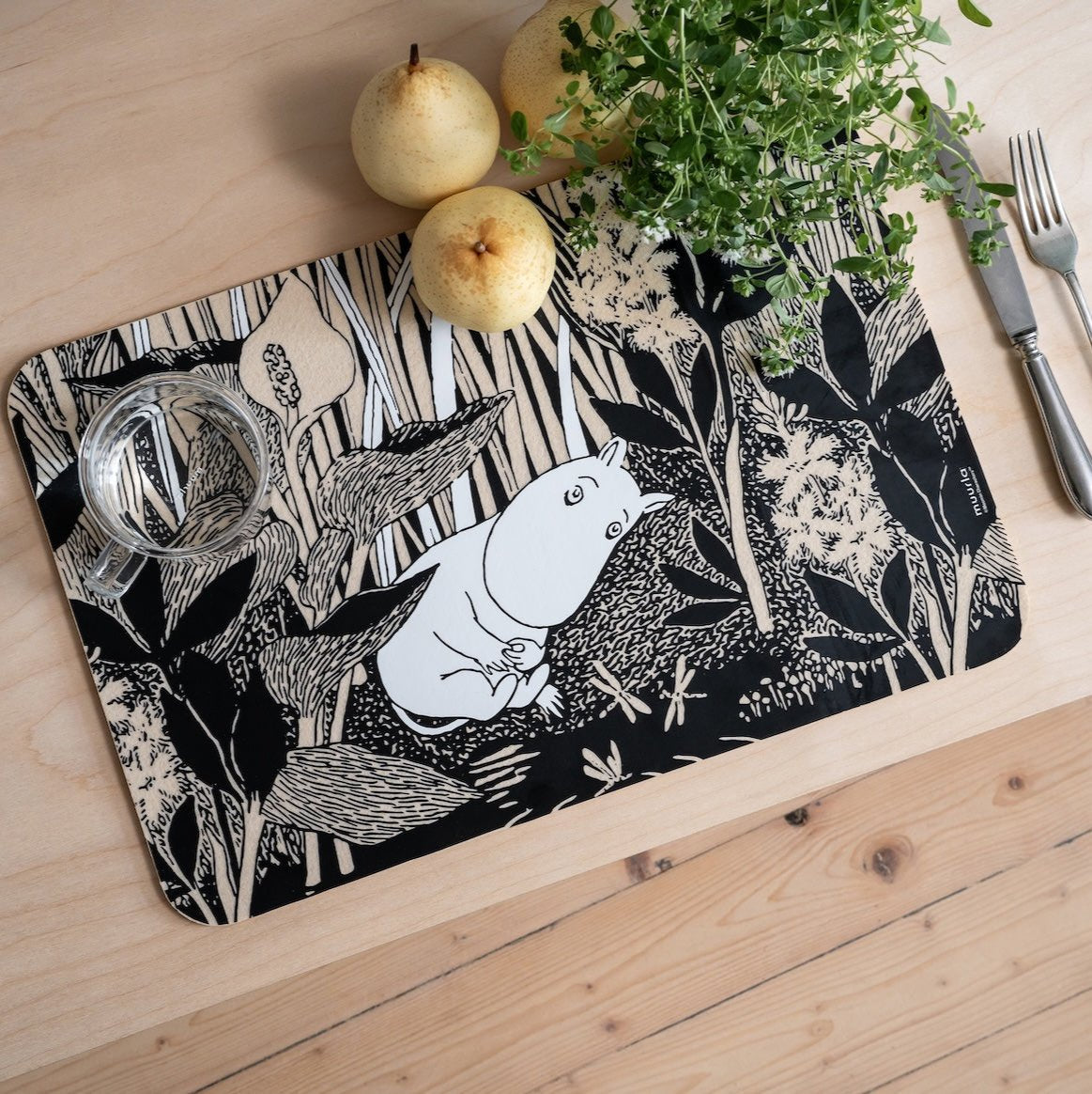 Moomin The Pond Placemat at a set table next to cutlery, herbs and fruit. 