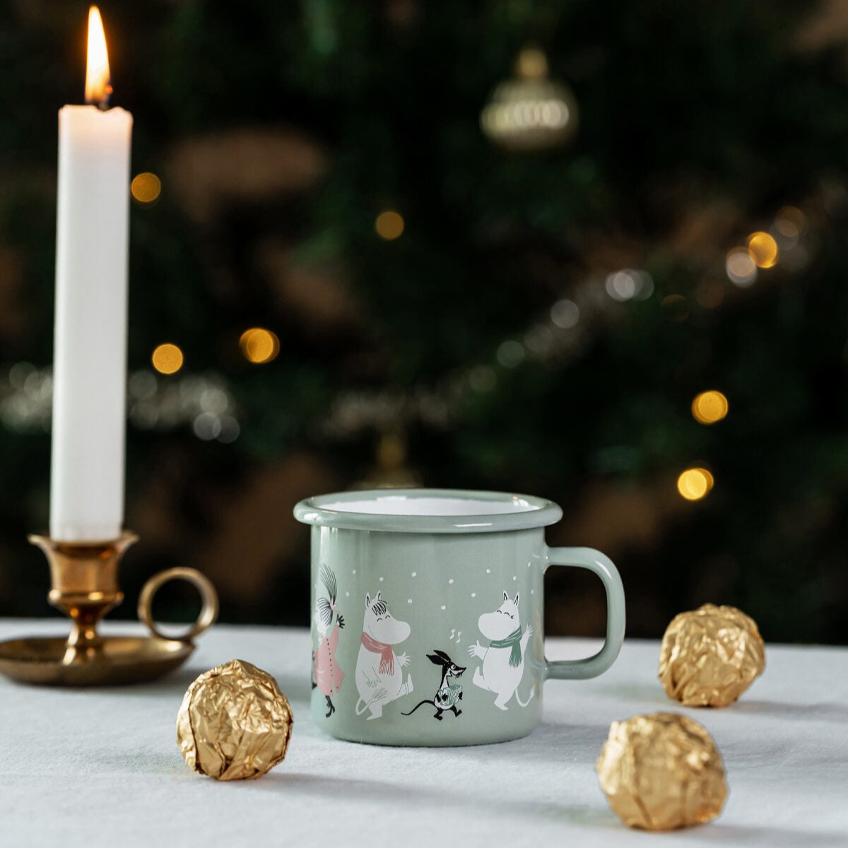 Muurla Moomin Festive Spirits Mug shown next to gold chocolates and a candle in an old style brass candle holders 