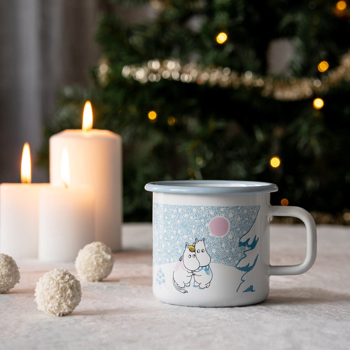 Moomin Let It Snow Mug by Muurla Design shown on a white tablecloth and with candles and a Christmas Tree behind