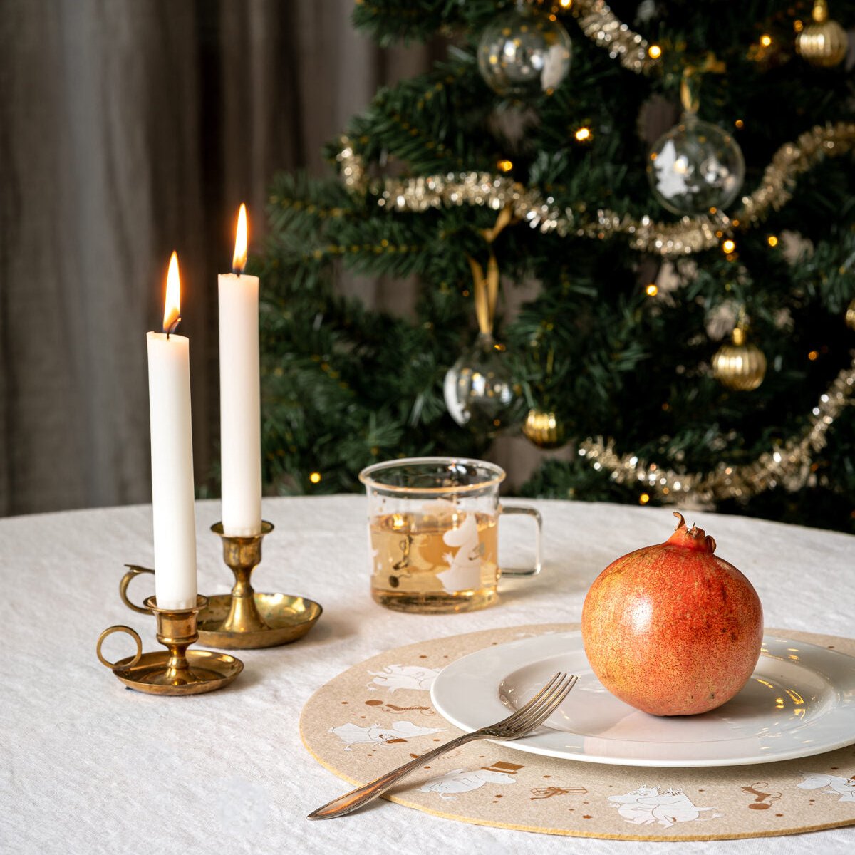 Muurla Sparkling Stars Placemat, on a table with a Christmas setting of candles and a decorated tree in the background.