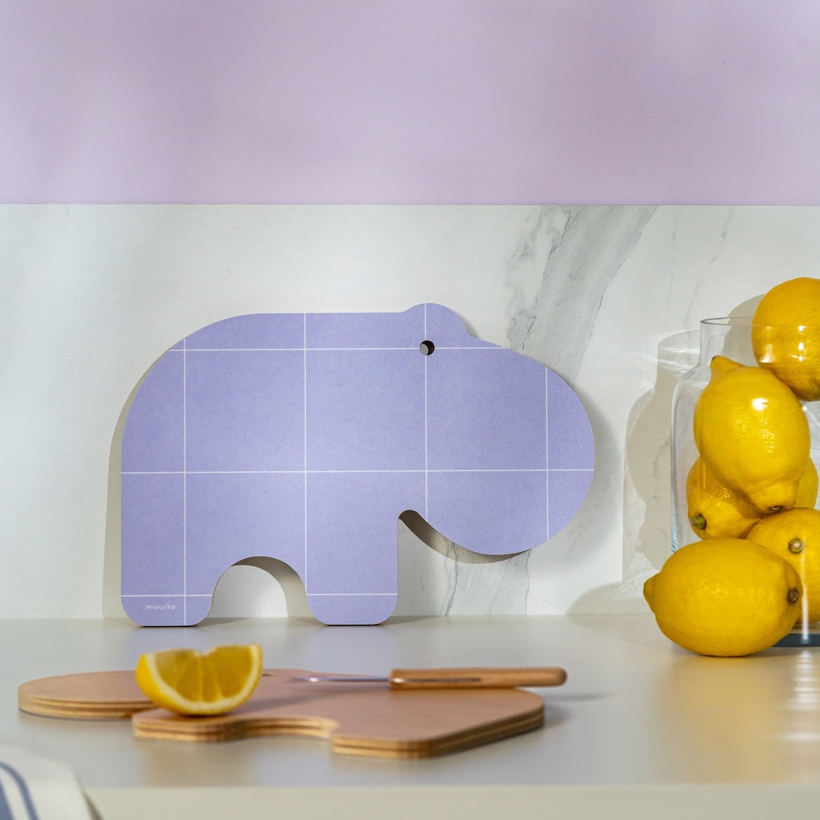 Purple hippo-shaped cutting board on a kitchen counter with lemons.