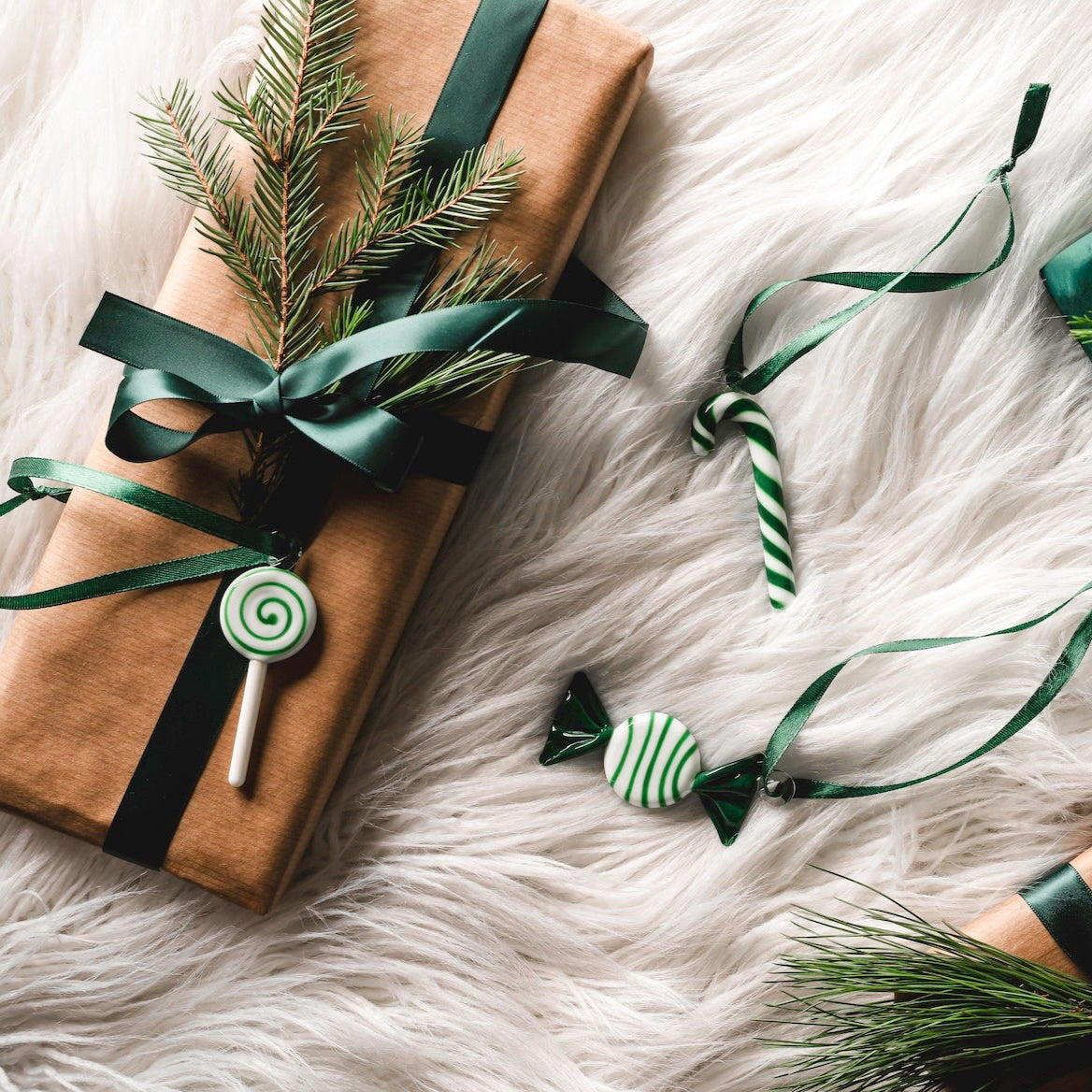 Gifts wrapped in brown paper with green ribbons and pine branches on a white fur surface.