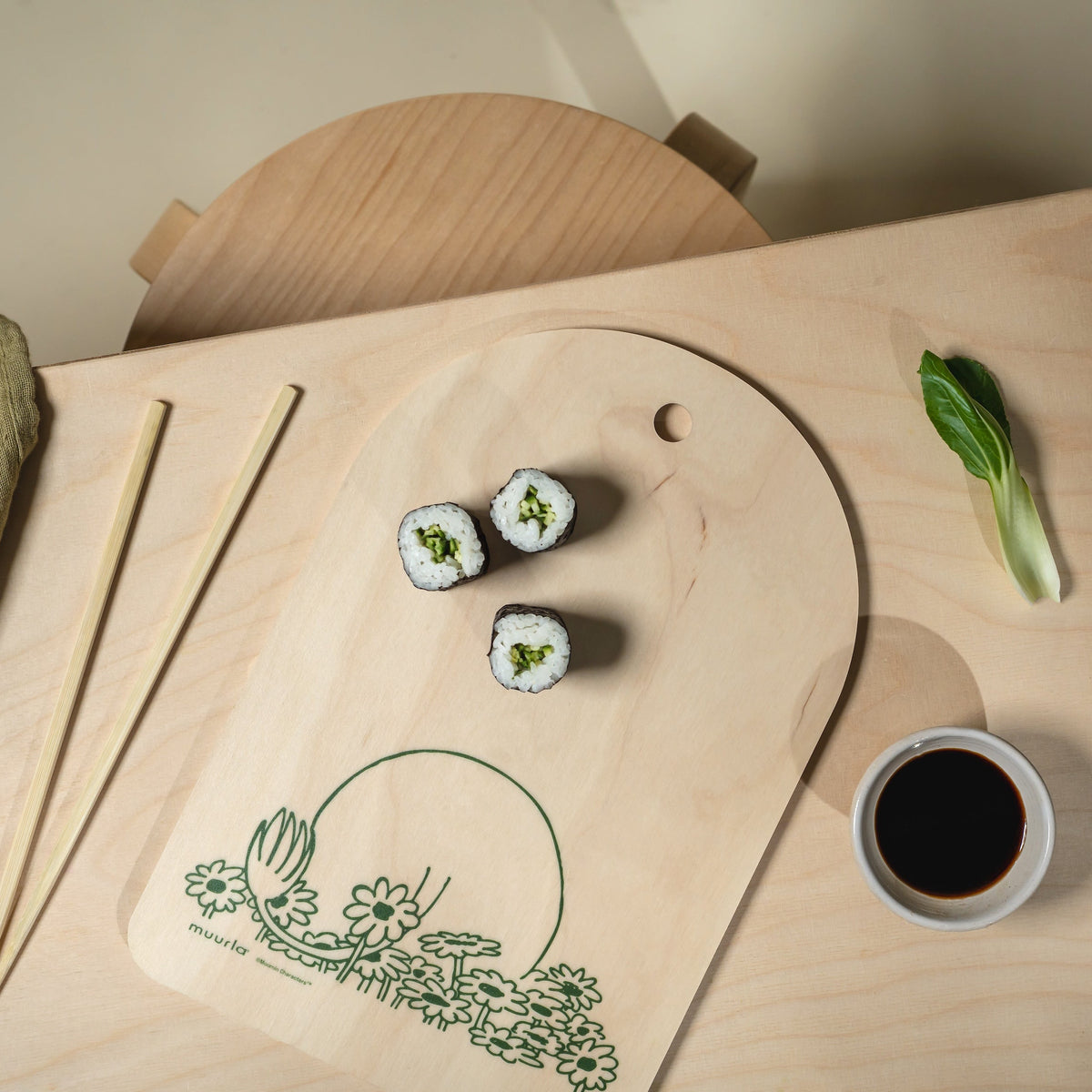 Three sushi rolls on a wooden board with a cup of soy sauce and a leafy green vegetable.