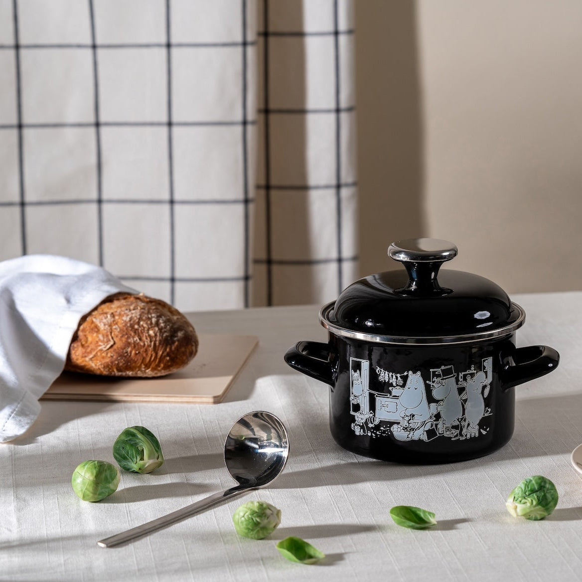 Moomin Cookware Enamel Pot by Muurla Design.   Shown on a dining table next to a ladle, fresh bread, and some sprouts! 