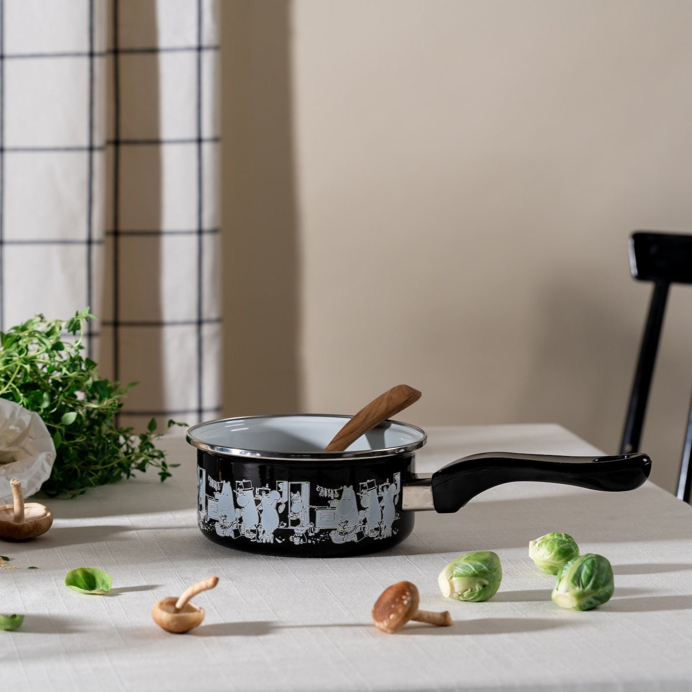 Muurla Moomin In The Kitchen Saucepan shown on a dining table with a wooden spoon sticking out of it, and with spouts and mushrooms around it.