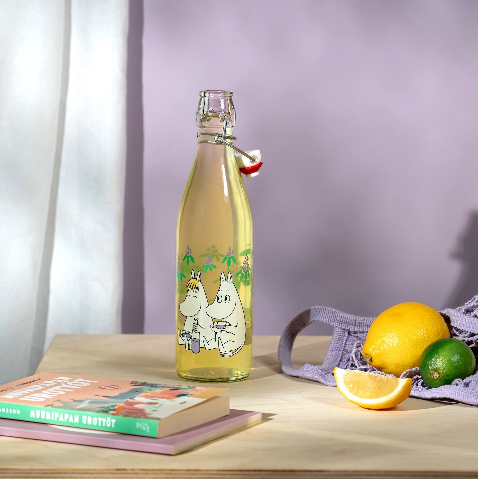 Bottle of lemonade with Moomin characters on a table with fruits and books