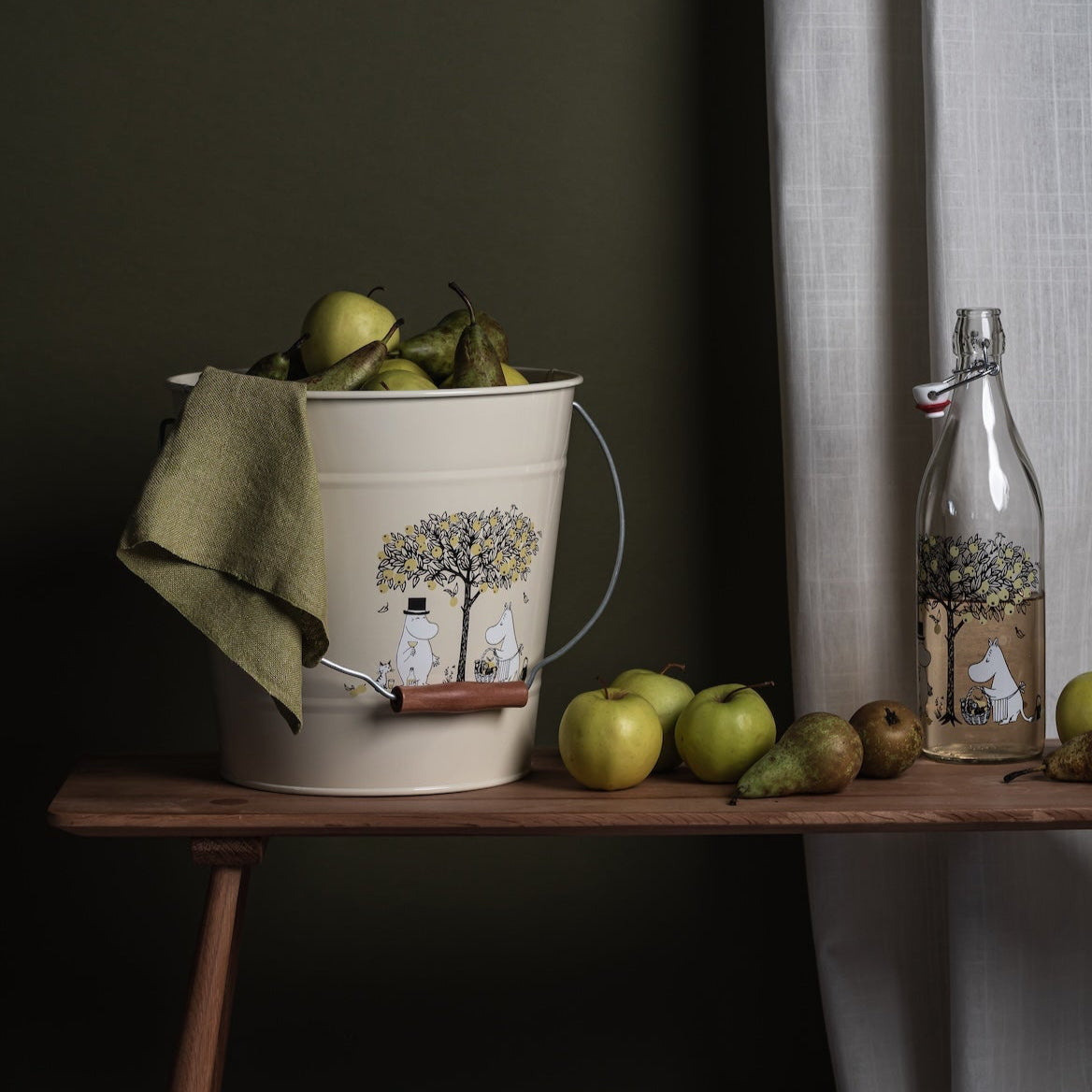 Moomin Apples Bucket shown on a hall table next to green apple and a glass bottle.