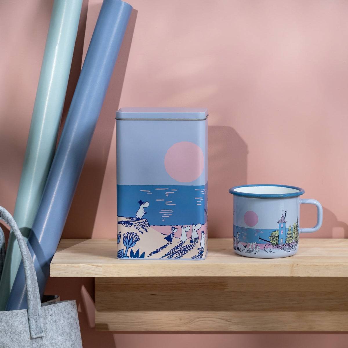 Decorative Moomin items with a scenic design on a shelf against a pink wall