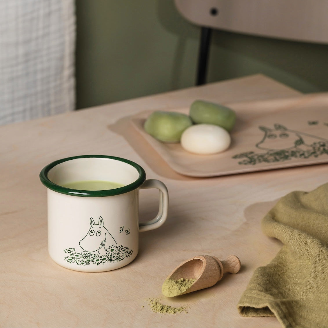 Moomin Mug Summer Crush with green design on a table next to a plate with green apples and a wooden scoop.