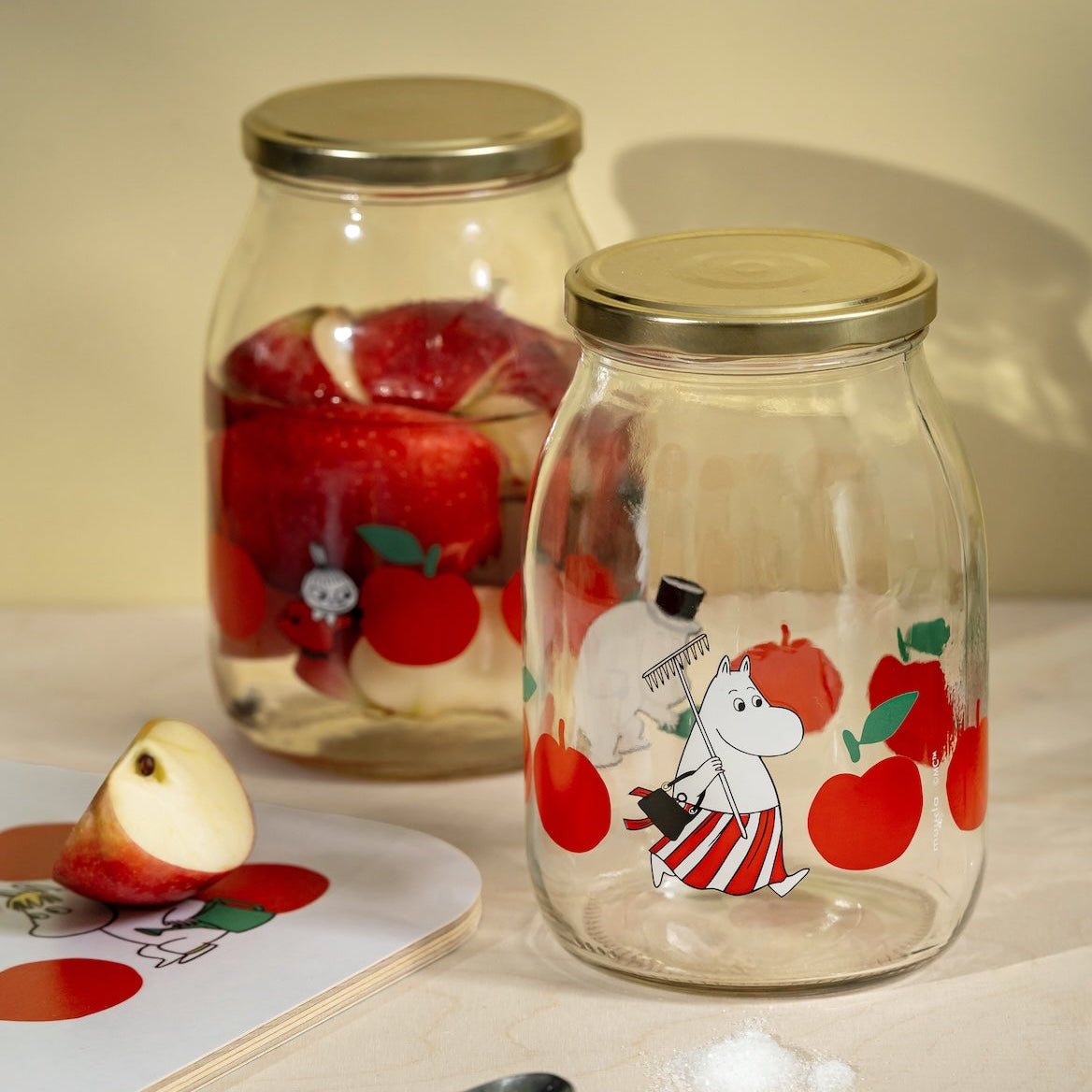 Two Moomin glass jars with cartoon character designs on a light surface.