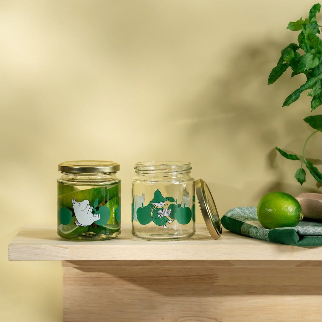 Two Moomin glass jars with floral designs on a wooden shelf against a yellow wall.