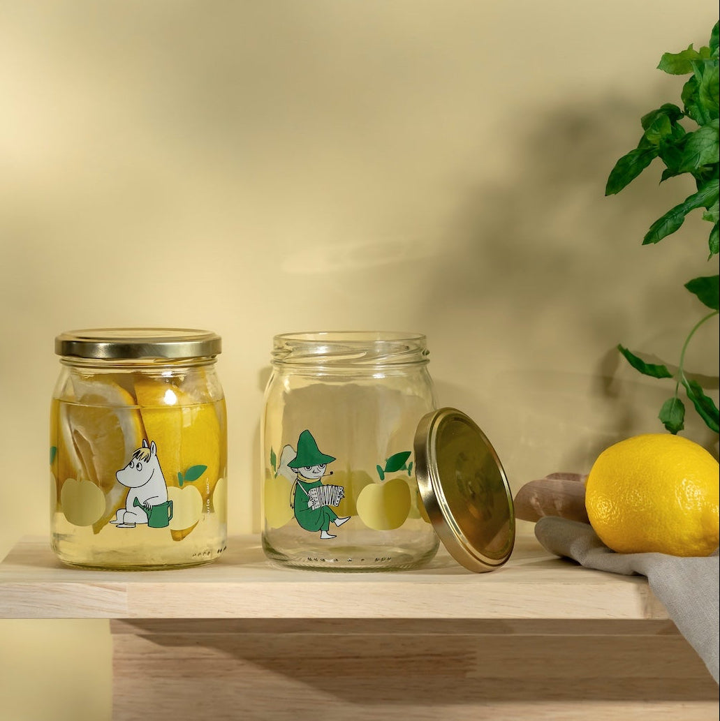 Two Moomin jars with lemon illustrations on a wooden shelf against a yellow background