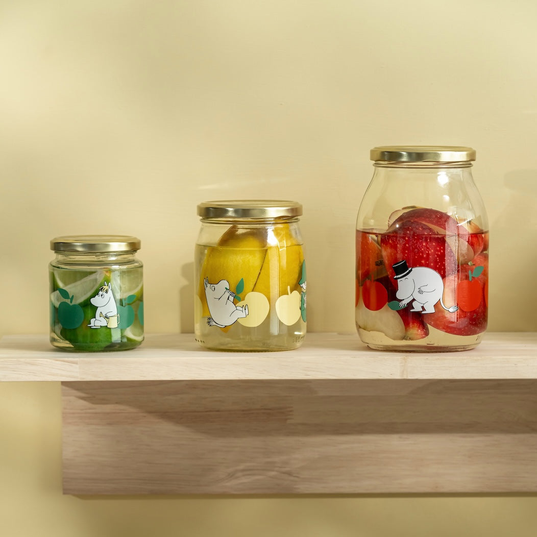Two Moomin jars with lemon illustrations on a wooden shelf against a yellow background