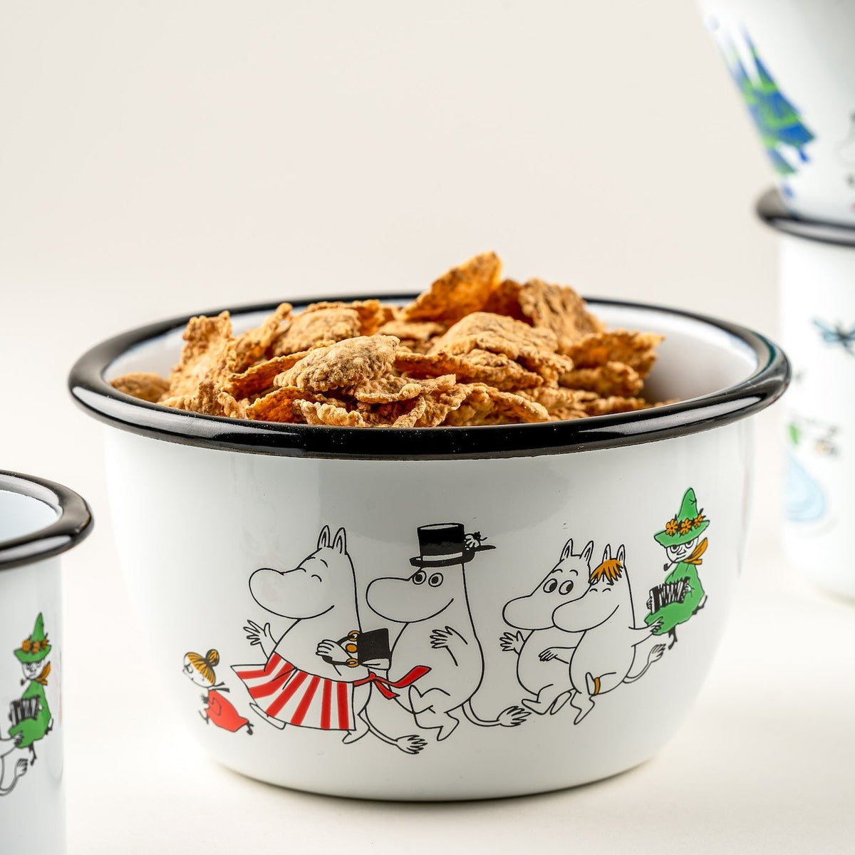 Moomin Valley Enamel Bowl by Muurla Design filled with cereal.   All the key Moomin Valley characters and landscapes are shown on the side of the bowl
