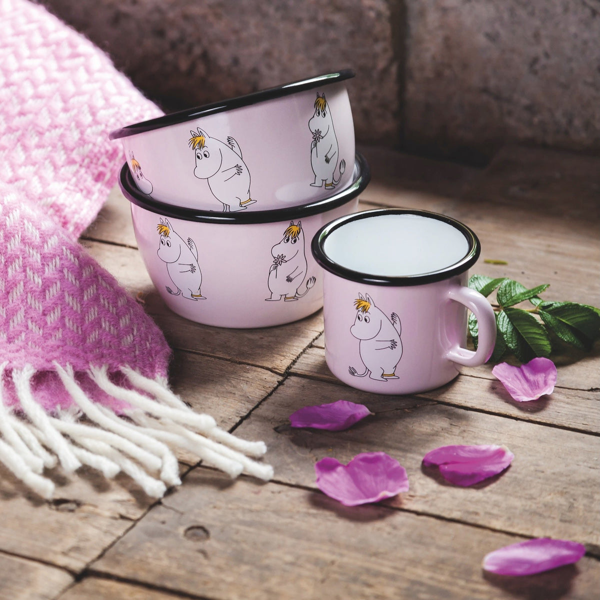 Snorkmaiden Enamel Mug and Bowl pictures next to a pink blanket and flower petals.  Moomin Retro Series of Enamelware by Muurla Design