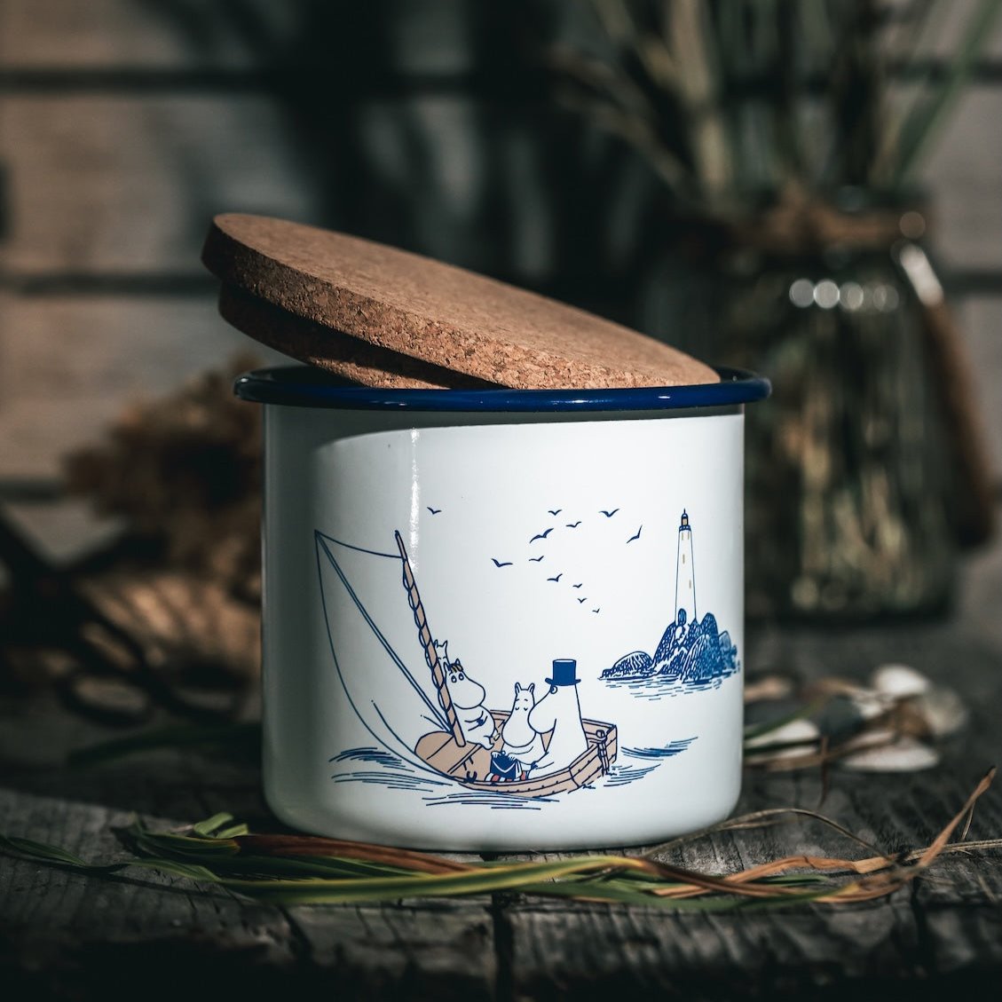 Moomin Sailors Enamel Jar with Cork Lid.  Shown with its Cork lid tilted, sitting on wood decking.