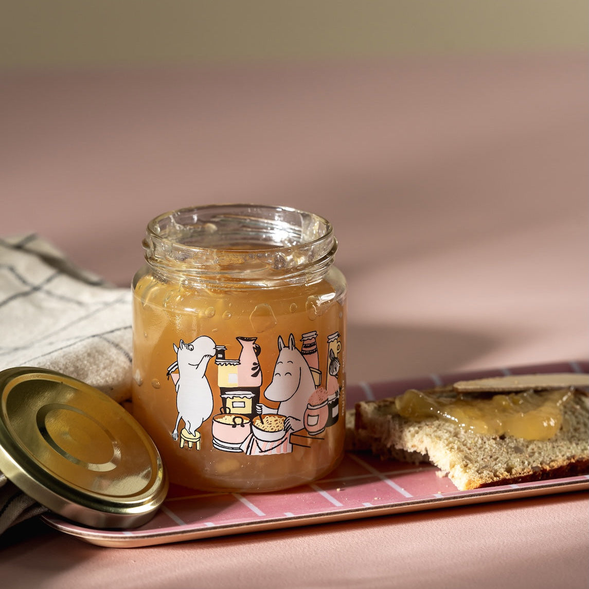 Moomin Glass Jar with metal lid.  Jam 0.3L shown full of jam,  on a pink tray with a slice of toast  next to it.