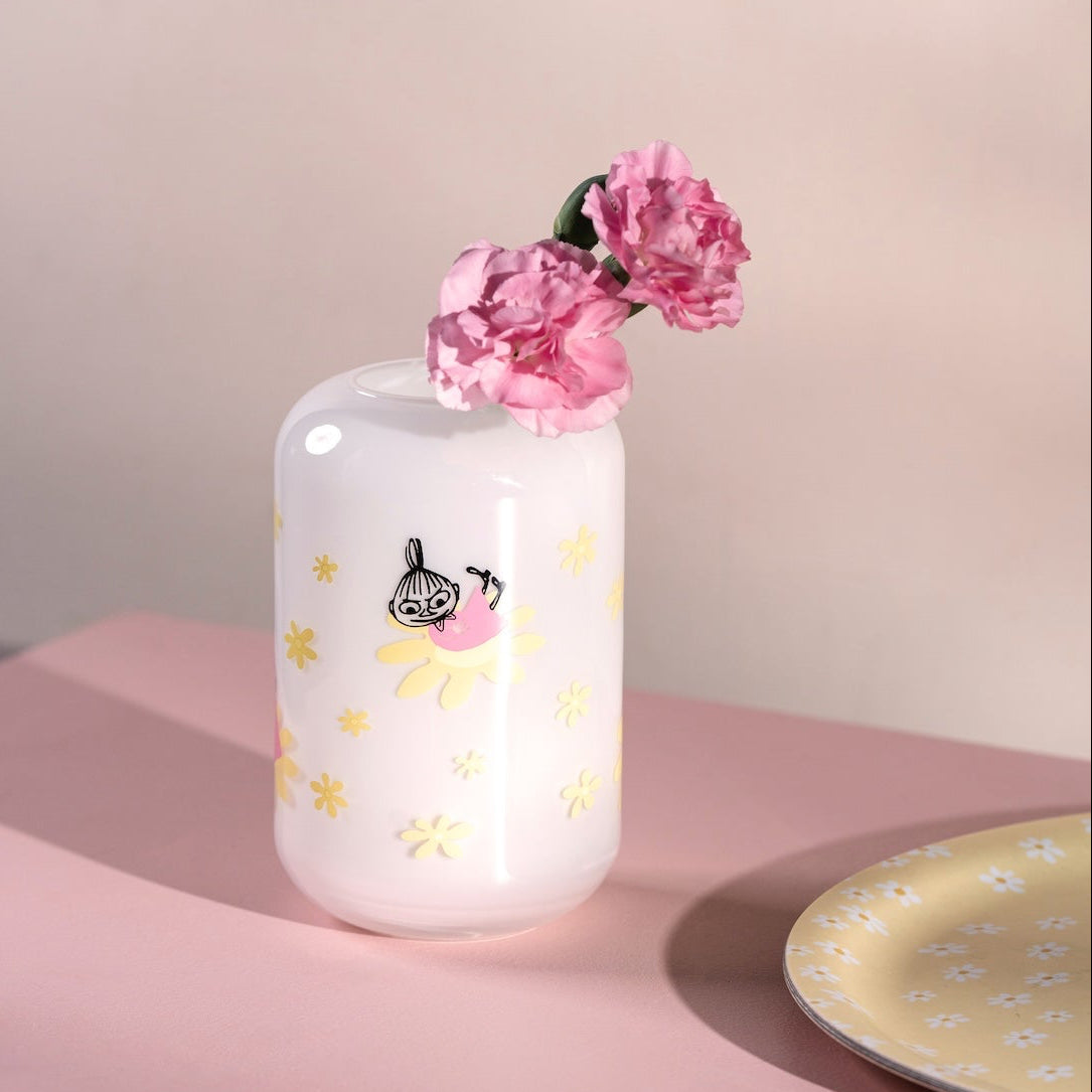 White Moomin vase with pink flowers on a pink surface with a light background