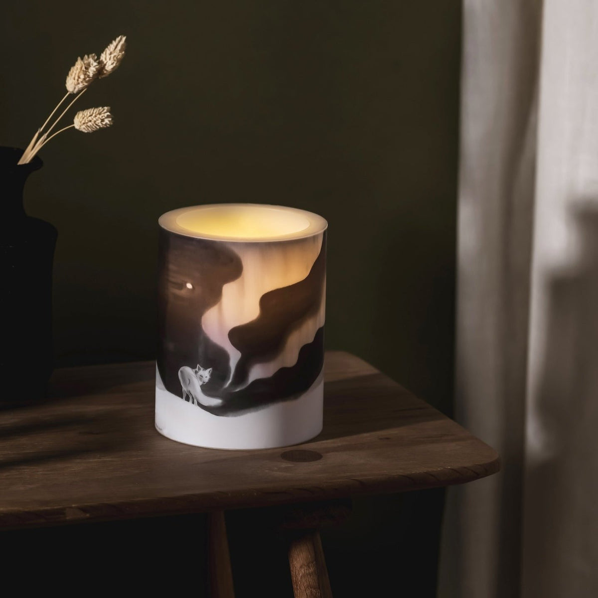 Teemu Jarvi Fox LED Candle.   Lit on a wooden table next to a vase.  Made by Muurla Design