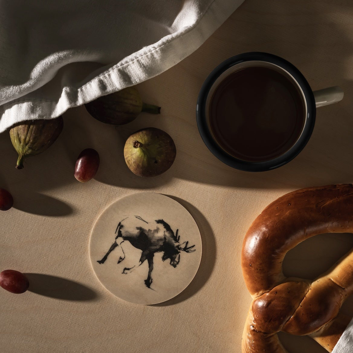 Moose Coaster by Teemu Jarvi on a table with fruit and a cup of coffee