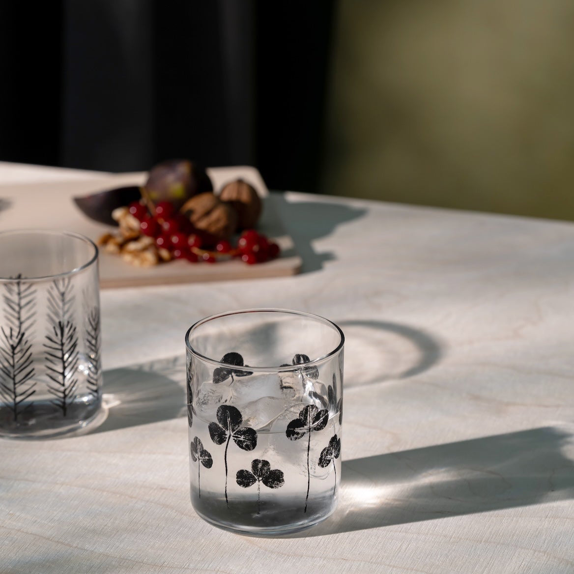 Clear glass with black clover design on a light surface with blurred background.  Made by Muurla Design