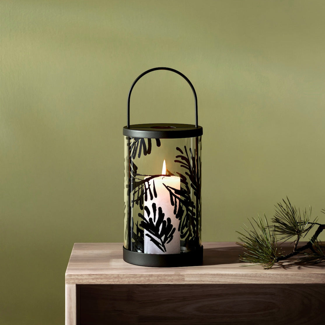 Decorative Teeum Jarvi  lantern with a candle on a wooden surface against a green wall