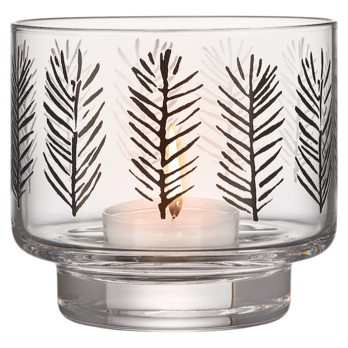 Clear glass candle holder with black leaf pattern containing a lit candle on a white background.  Teemu Jarvi