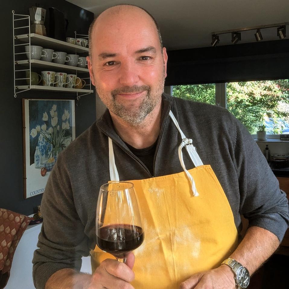 Laurence White - owner of Treacle George, and 'Tipsy' Hobby Cook - holding a glass of red wine and wearing a yellow apron with flour on it.