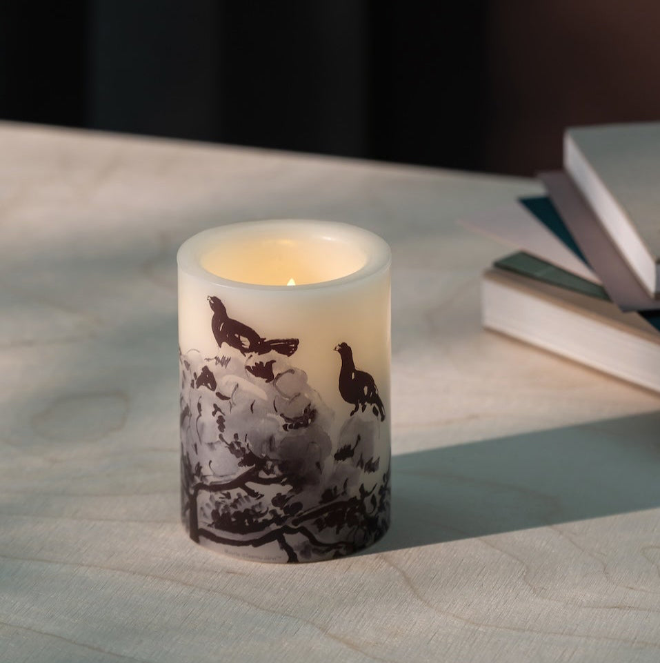 Flickering LED Capercaillie candle on a table with books in the background. Teemu Jarvi Design
