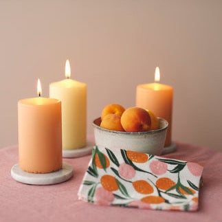 Havi Paper Napkins in Nectarine.  On a table with lit orange candles and a bowl of nectarines 