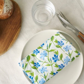 Linnea Blue Paper Napkins by Havi, placed on a white dinner plate with cutlery and a glass alongside