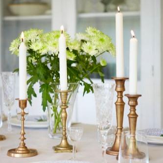 Elegant dining table with white plates, crystal glasses, brass candlesticks, lit Havi Crown candles, and a vase of green chrysanthemums.