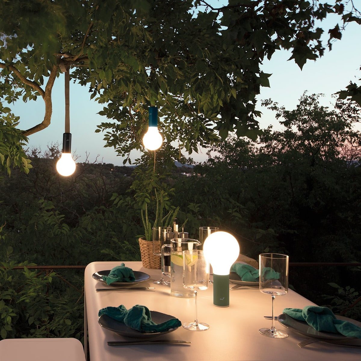 Fermob Aplo lamps on a table and also hanging from a tree with the Aplo Suspension Strap