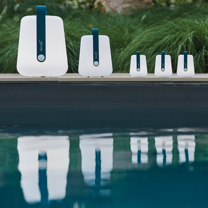 Fermob Balad lamps, all in Acapulco Blue, placed along a swimming pool edge, and reflecting in the pool