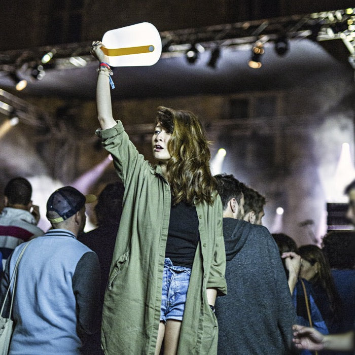A girl at a festival holding up a Fermob Balad Lamp with a Honey Yellow Handle 