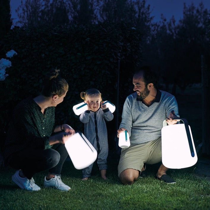 Young family smiling in the garden holding Balad Lamps of different sizes.