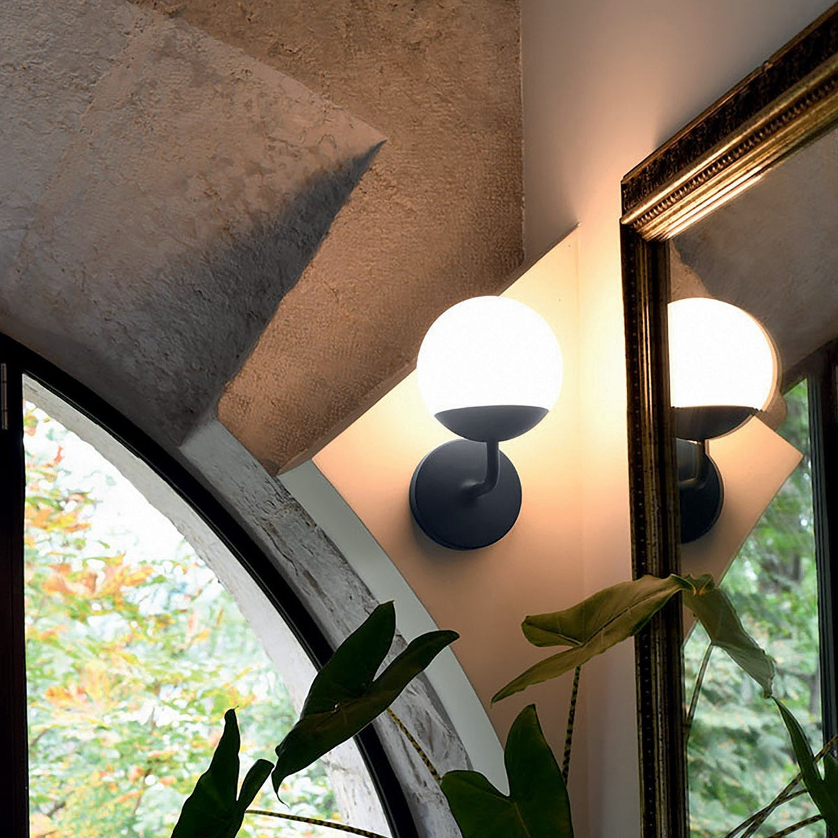 The Fermob Mooon! Wall Lamp in Anthracite.   Fixed to a garden room wall, surrounded by windows and greenery.
