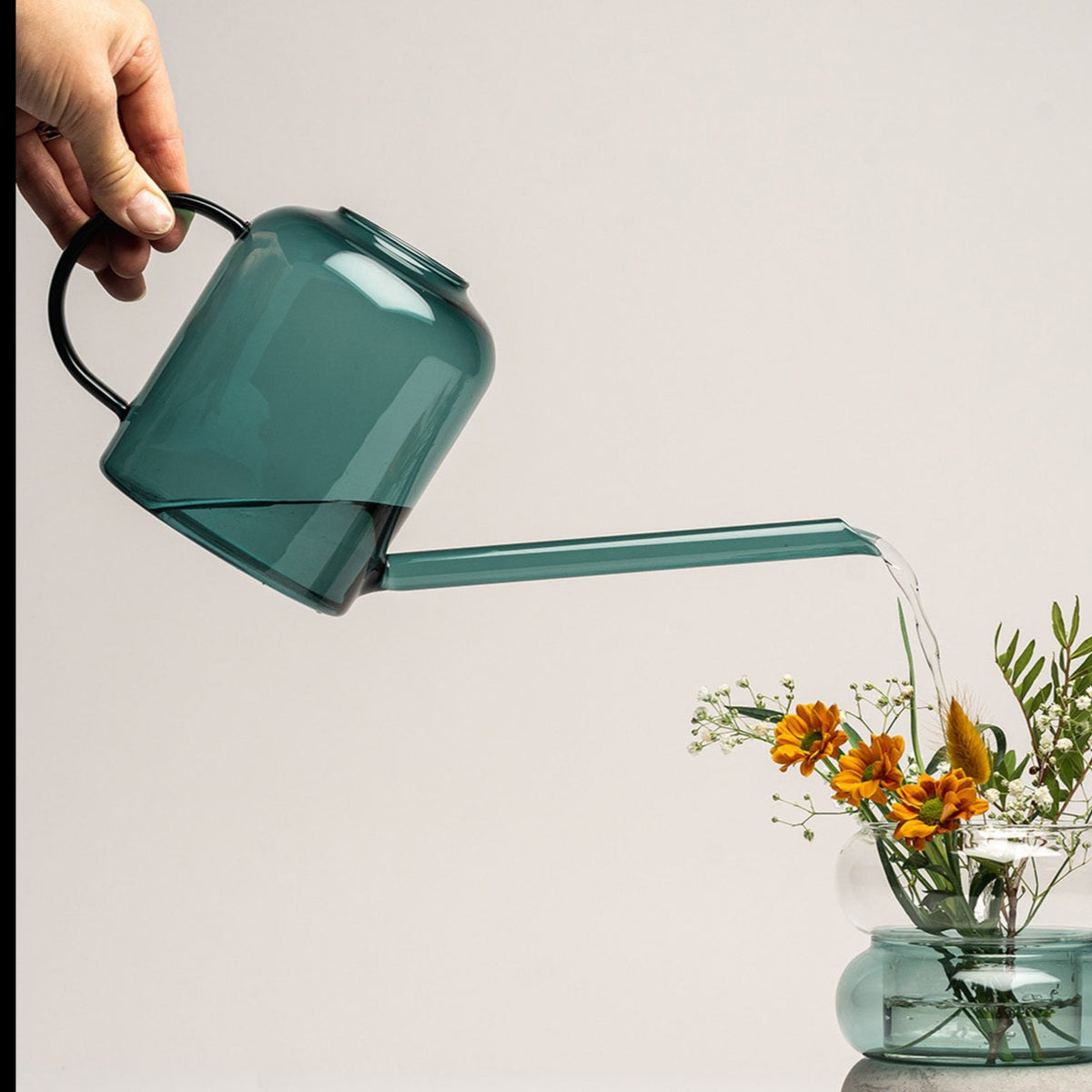 Water being poured from a Muurla Design Watering Can made in Borosilicate Glass. Teal Colourway 